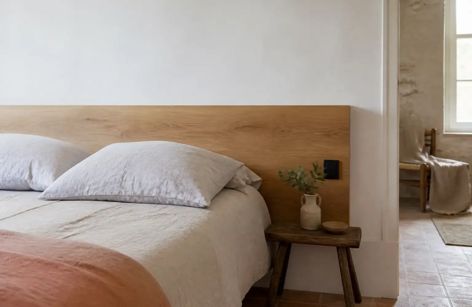 Chambre à coucher avec une tête de lit en bois clair fixée contre un mur blanc