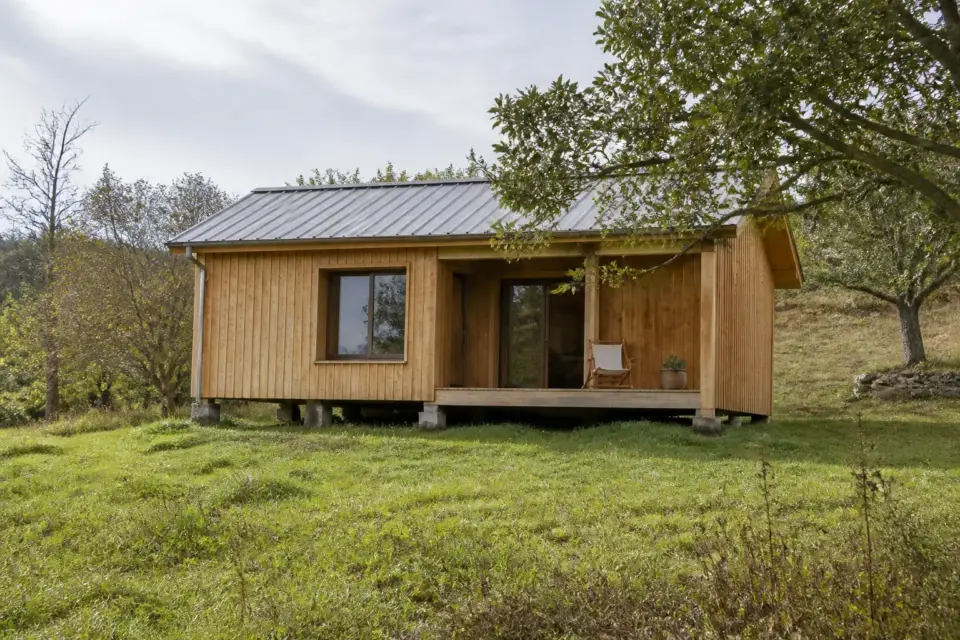 Petite maison en bois posée sur des fondations au milieu d’un terrain dégagé