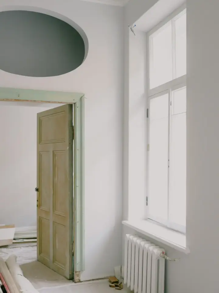 Pièce en cours de rénovation : porte ancienne, fenêtre neuve, radiateur et murs blancs