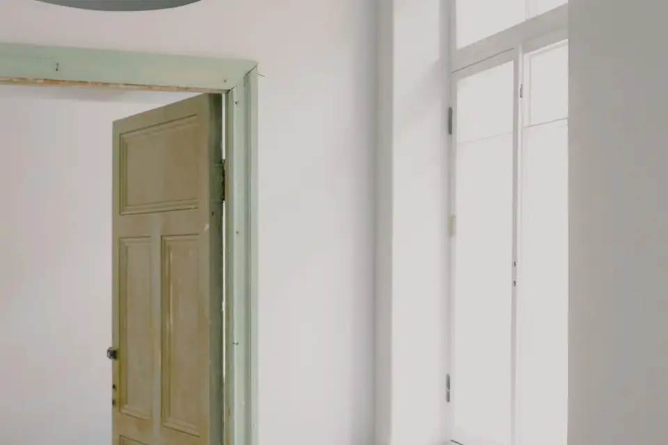 Pièce en cours de rénovation : porte ancienne, fenêtre neuve, radiateur et murs blancs